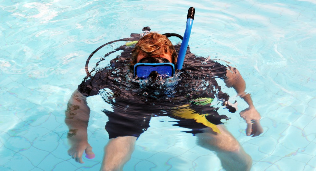 Happy scuba diver in the swimming pool blowing bubbles.