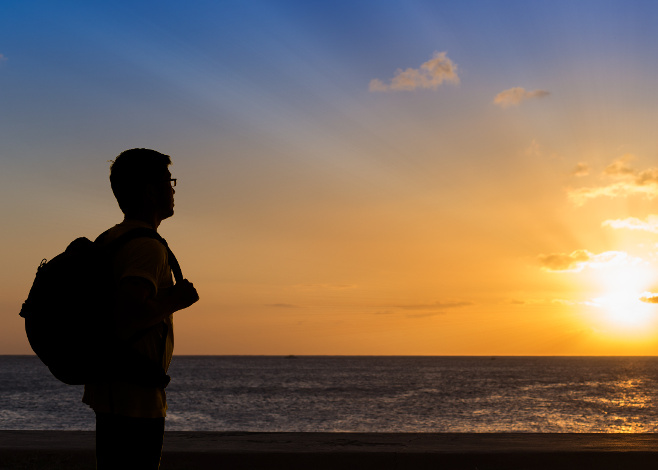 Silhouette traveler with backpack standing near the beach at sunset