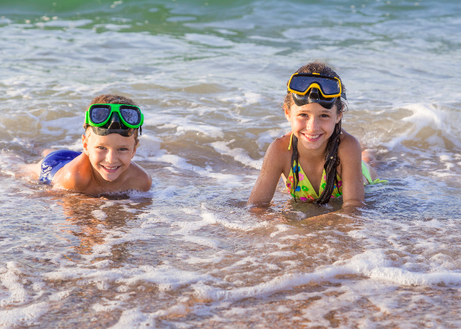 Two happy kids in diving masks swim in the surf