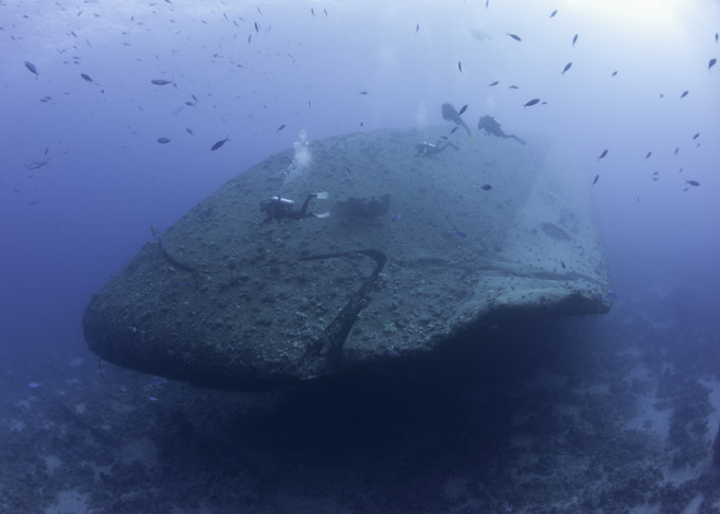 Scuba divers exploring a large sunken underwater shipwreck