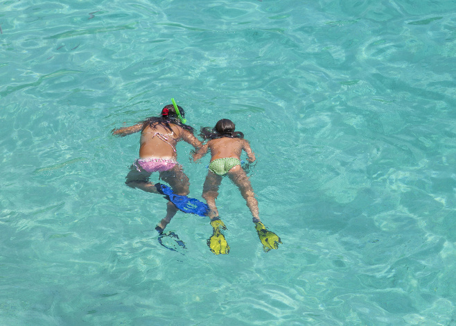Two girls swimming while wearing snorkeling gear in water