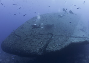 Scuba divers exploring a large sunken underwater shipwreck
