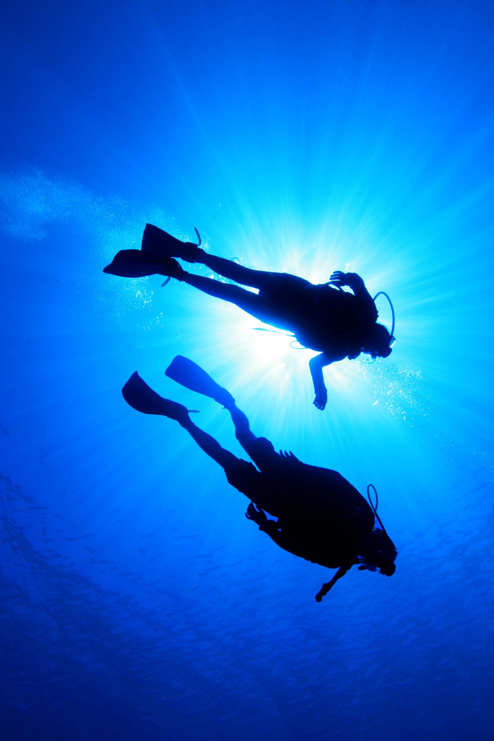 Two scuba divers silhouetted against sunrays in deep blue water